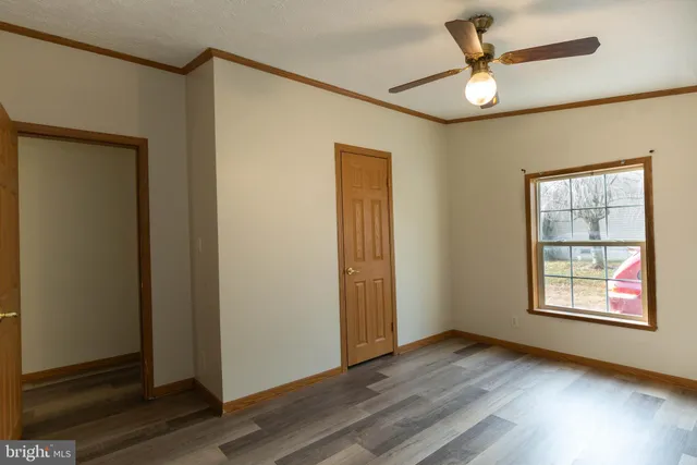 an empty room with wooden floor fan and windows