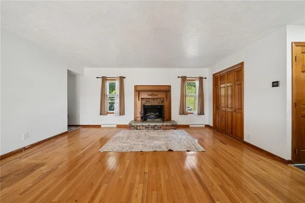 an empty room with wooden floor fireplace and windows