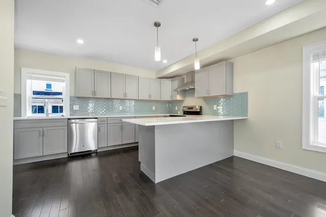 a kitchen with stainless steel appliances white cabinets a sink a window and wooden floors