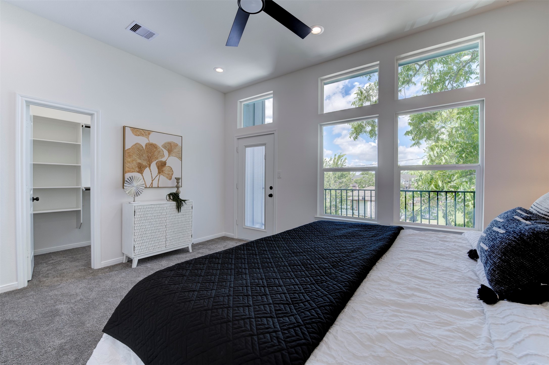 6807 Paris Street Houston, TX 77021 - Photo 28 of 50 Primary bedroom showing private balcony door, large windows with tree views, ceiling fan, carpet, and open walk-in closet with built-in shelving.
