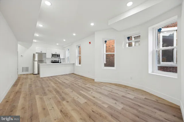 a view of empty room with wooden floor and kitchen