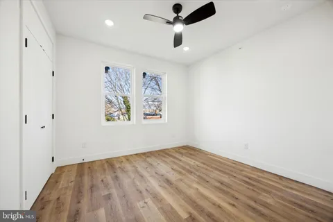 an empty room with wooden floor ceiling fan and windows