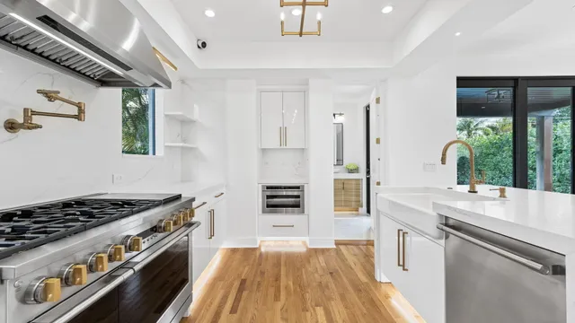 a kitchen with stainless steel appliances granite countertop a refrigerator a stove a sink and white cabinets with wooden floor next to windows