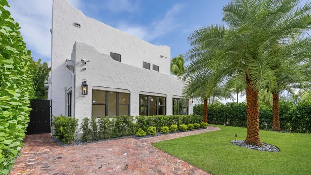 a palm tree sitting in front of a house with a yard and palm trees