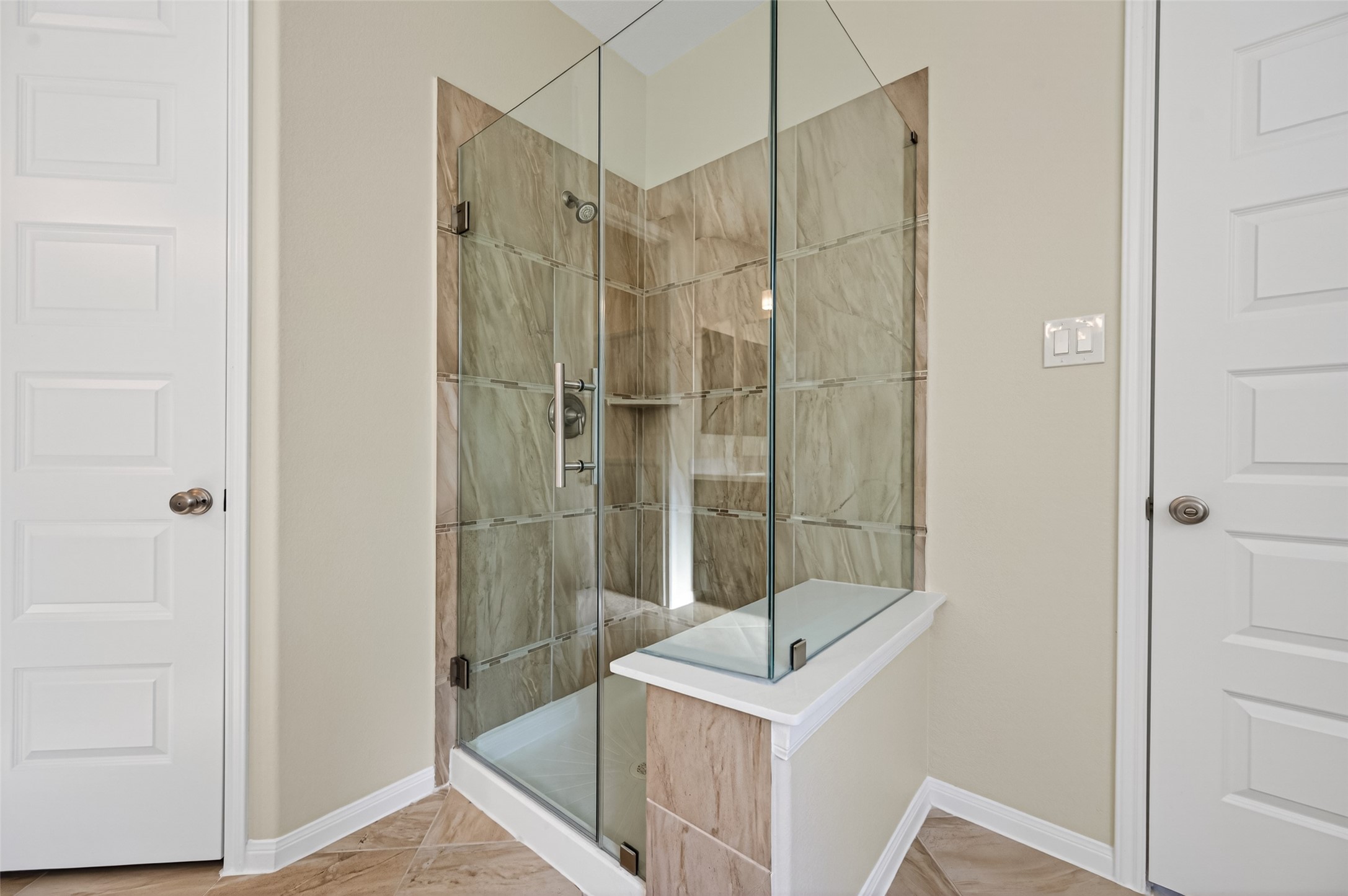 7003 Bristol Memorial Drive Spring, TX 77379 - Photo 24 of 40 Glass-enclosed primary shower in this Spring TX 77379 home featuring full-height tile surround, decorative accent banding, and built-in corner shelving. The frameless glass design enhances openness while highlighting the neutral stone-look tile finishes. Positioned within the spacious primary bathroom, this walk-in shower adds a clean, modern touch and complements the home’s move-in ready appeal near The Woodlands.