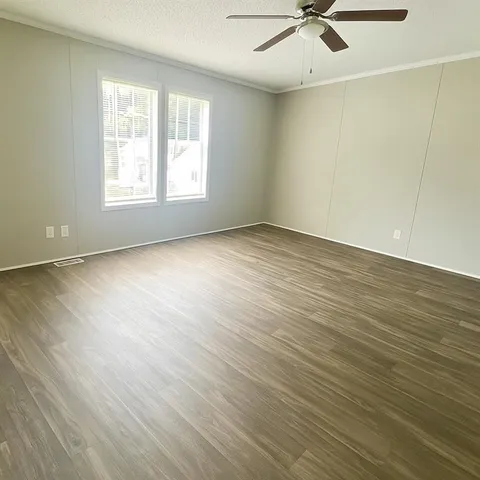 an empty room with wooden floor fan and windows