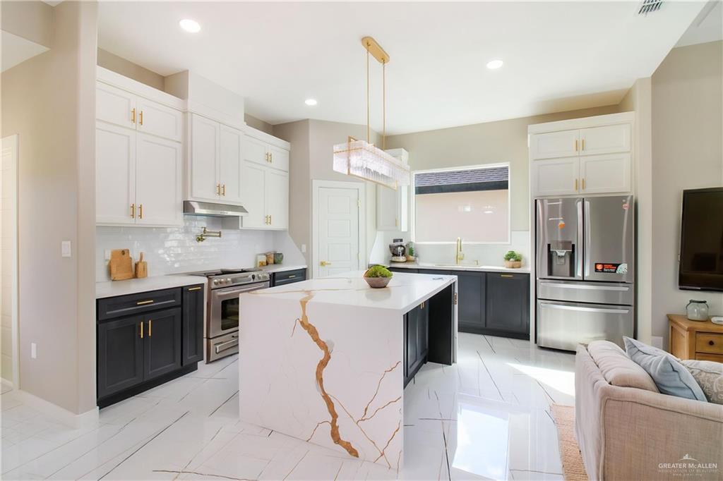 909 Azalea Street Mission, TX 78573 - Photo 29 of 29 Kitchen featuring stainless steel appliances, two tone color scheme, open floor plan, light stone countertops, and a center island. Faucett on top of the stove to easy fill the pots
