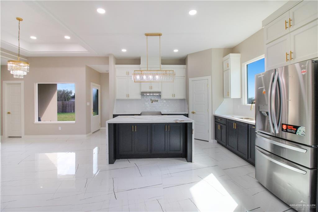 909 Azalea Street Mission, TX 78573 - Photo 2 of 29 Spacious Kitchen with stainless steel fridge with ice dispenser, two tone color scheme, hanging lights, a kitchen island, and light marble finish flooring