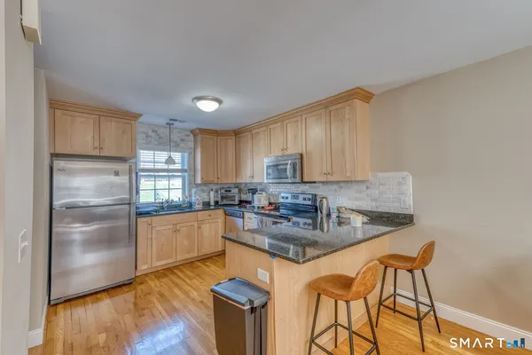 a kitchen with stainless steel appliances granite countertop a refrigerator a sink dishwasher a stove with wooden cabinets and floor