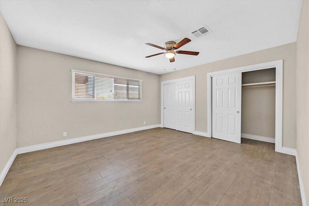 6384 West Desert Inn Road Las Vegas, NV 89146 - Photo 11 of 26 Unfurnished bedroom featuring two closets, a ceiling fan, and light wood-style flooring