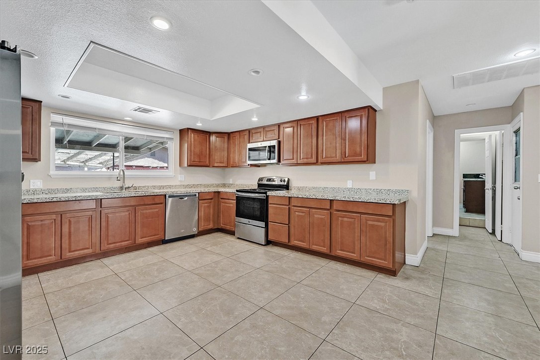 6384 West Desert Inn Road Las Vegas, NV 89146 - Photo 4 of 26 Kitchen featuring brown cabinets, appliances with stainless steel finishes, light tile patterned flooring, light stone counters, and recessed lighting