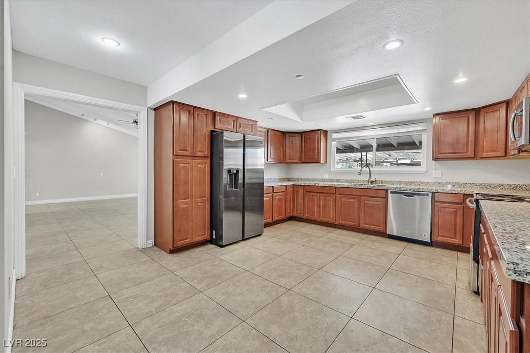 6384 West Desert Inn Road Las Vegas, NV 89146 - Photo 5 of 26 Kitchen featuring brown cabinets, light tile patterned flooring, stainless steel appliances, light stone counters, and recessed lighting