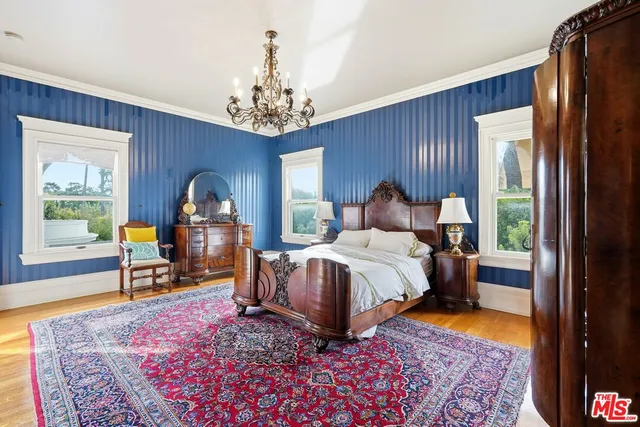 a bedroom with a bed table and two windows