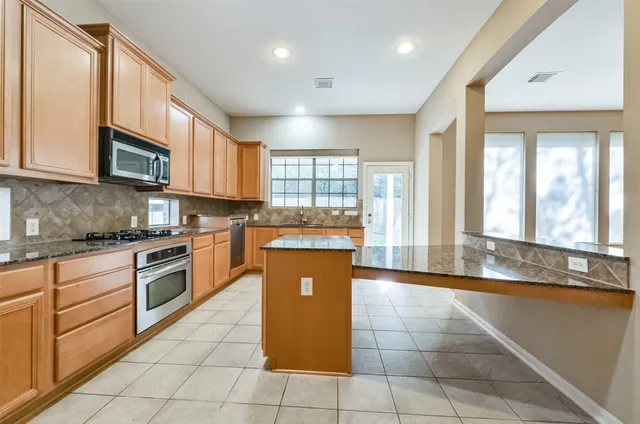 a large kitchen with stainless steel appliances granite countertop a stove a sink and a microwave