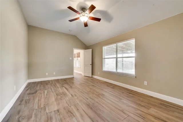 an empty room with wooden floor ceiling fan and windows
