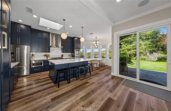 a kitchen with stainless steel appliances granite countertop a refrigerator a sink dishwasher a stove and a dining table with wooden floor