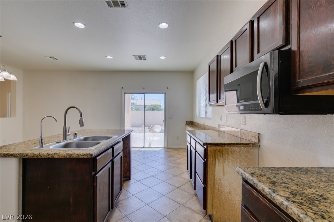 5150 Riverside Run Court North Las Vegas, NV 89081 - Photo 33 of 50 A functional kitchen boasts granite countertops and ample dark wood cabinetry, flowing seamlessly to an outdoor space.