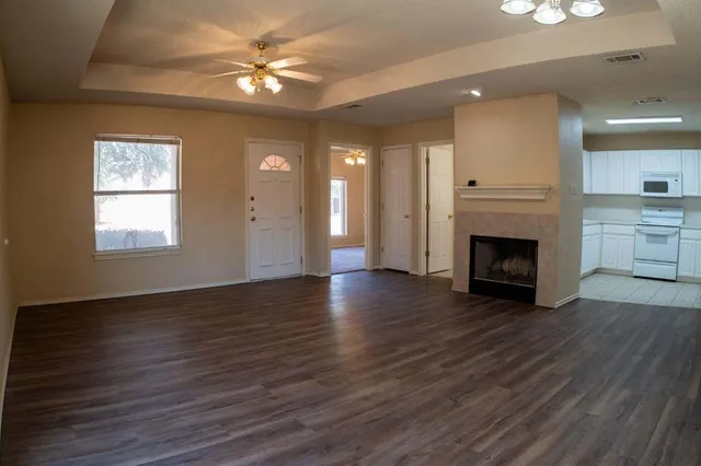 an empty room with wooden floor a ceiling fan a fireplace and windows