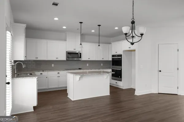 a kitchen with stainless steel appliances granite countertop a sink a stove a refrigerator and white cabinets with wooden floor