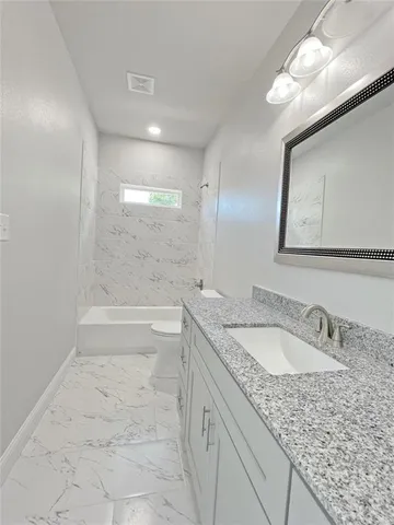 a bathroom with a granite countertop sink a toilet a mirror and bathtub