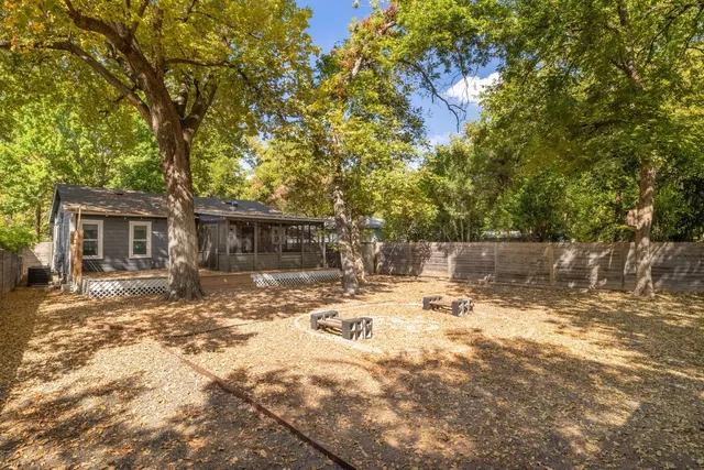 a backyard of a house with table and chairs under an large trees