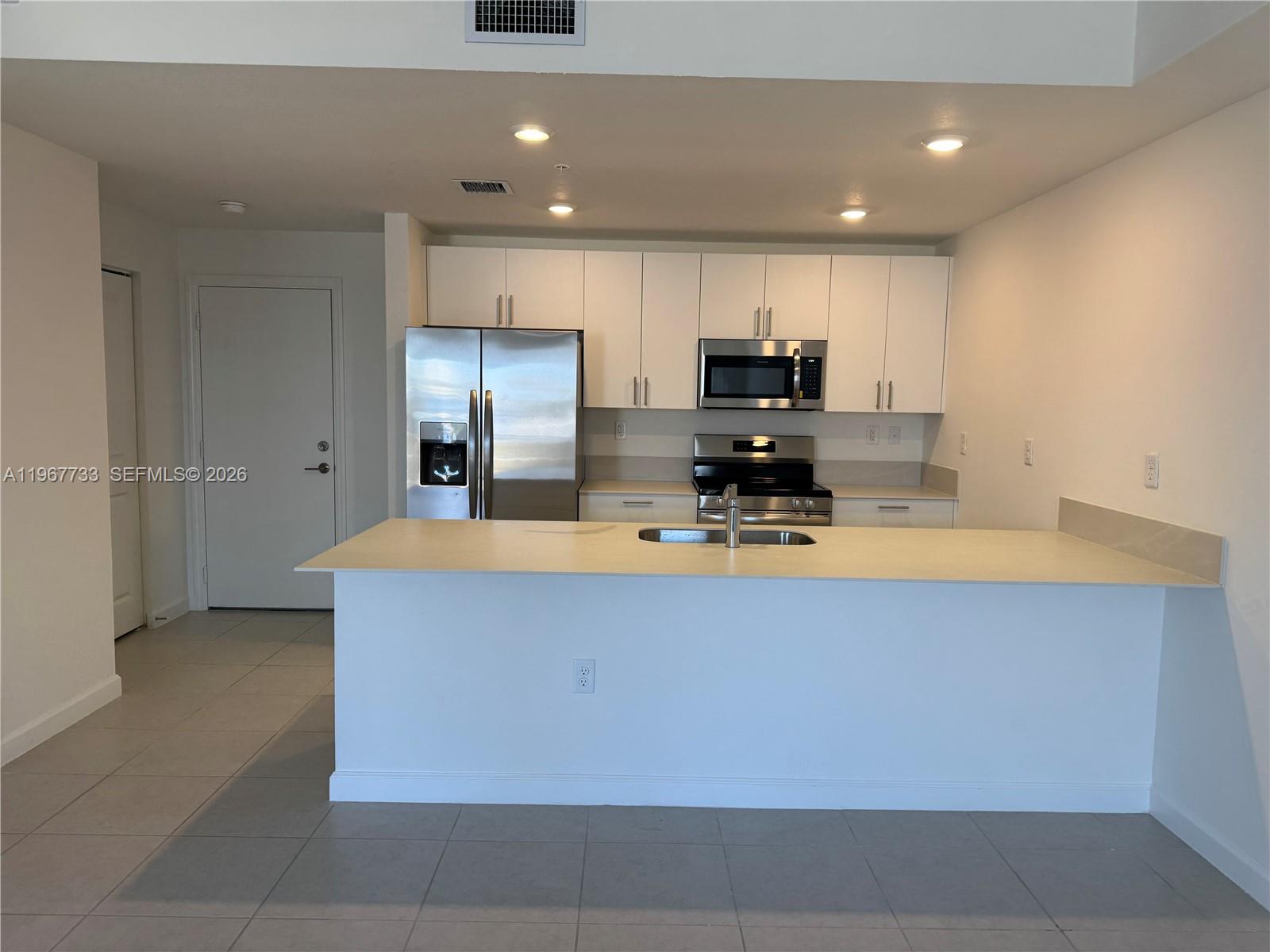 12420 Southwest 248th Street, Unit 7 Homestead, FL 33032 - Photo 6 of 31 a large kitchen with kitchen island granite countertop a refrigerator a stove and a sink with wooden cabinets