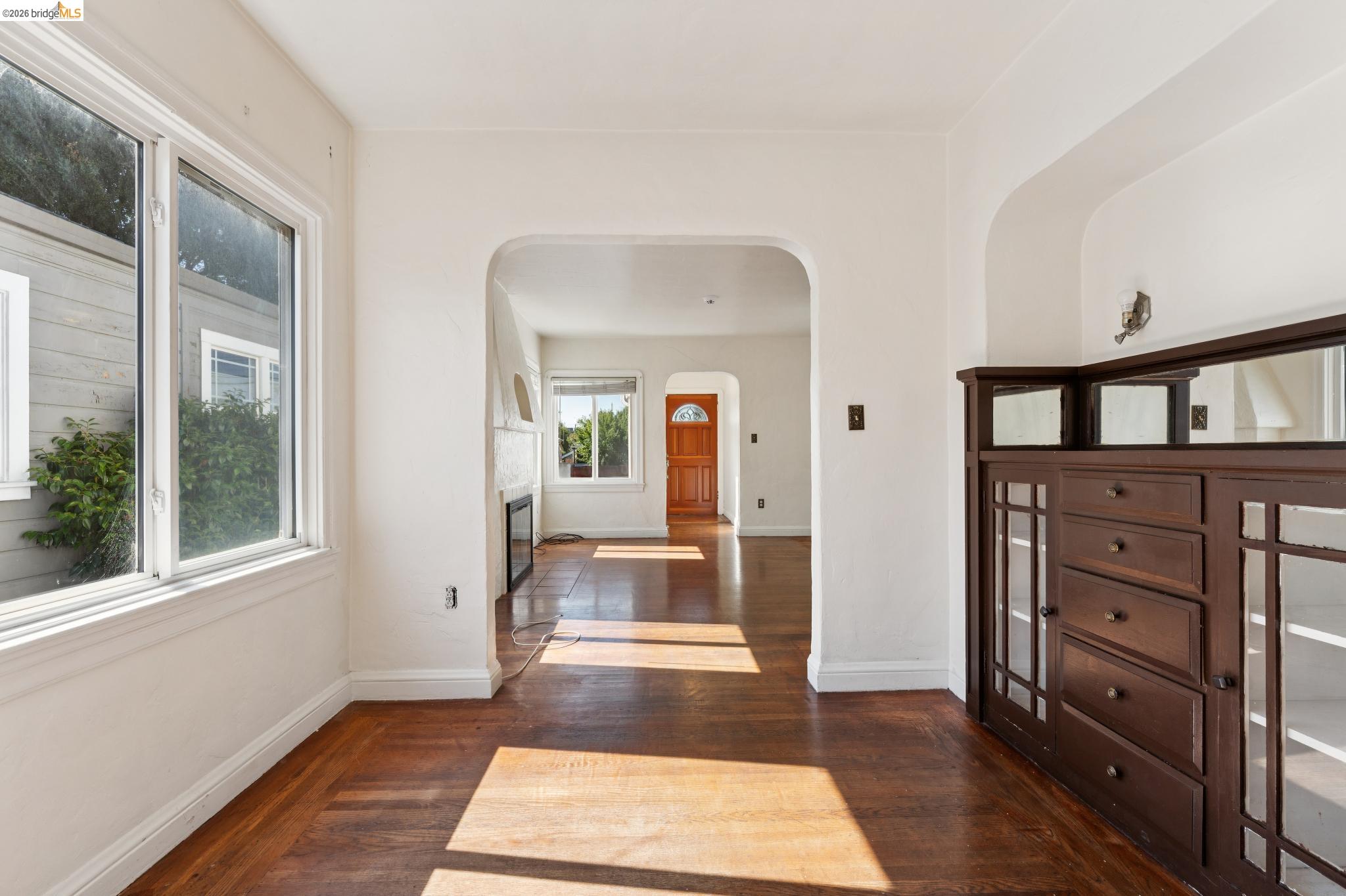 978 43rd Street Oakland, CA 94608 - Photo 14 of 46 Wood-finish flooring extends throughout this interior space, featuring a built-in dark wood cabinet with glass-paned doors and drawer storage