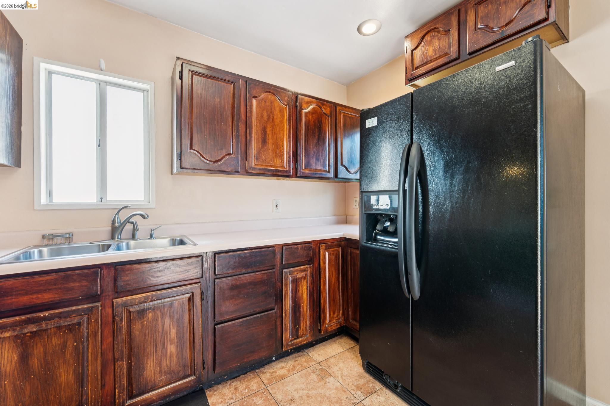 978 43rd Street Oakland, CA 94608 - Photo 19 of 46 Kitchen featuring wood-finish cabinetry, light-toned countertops, a double basin sink with a chrome faucet, a white-framed window, and tile flooring