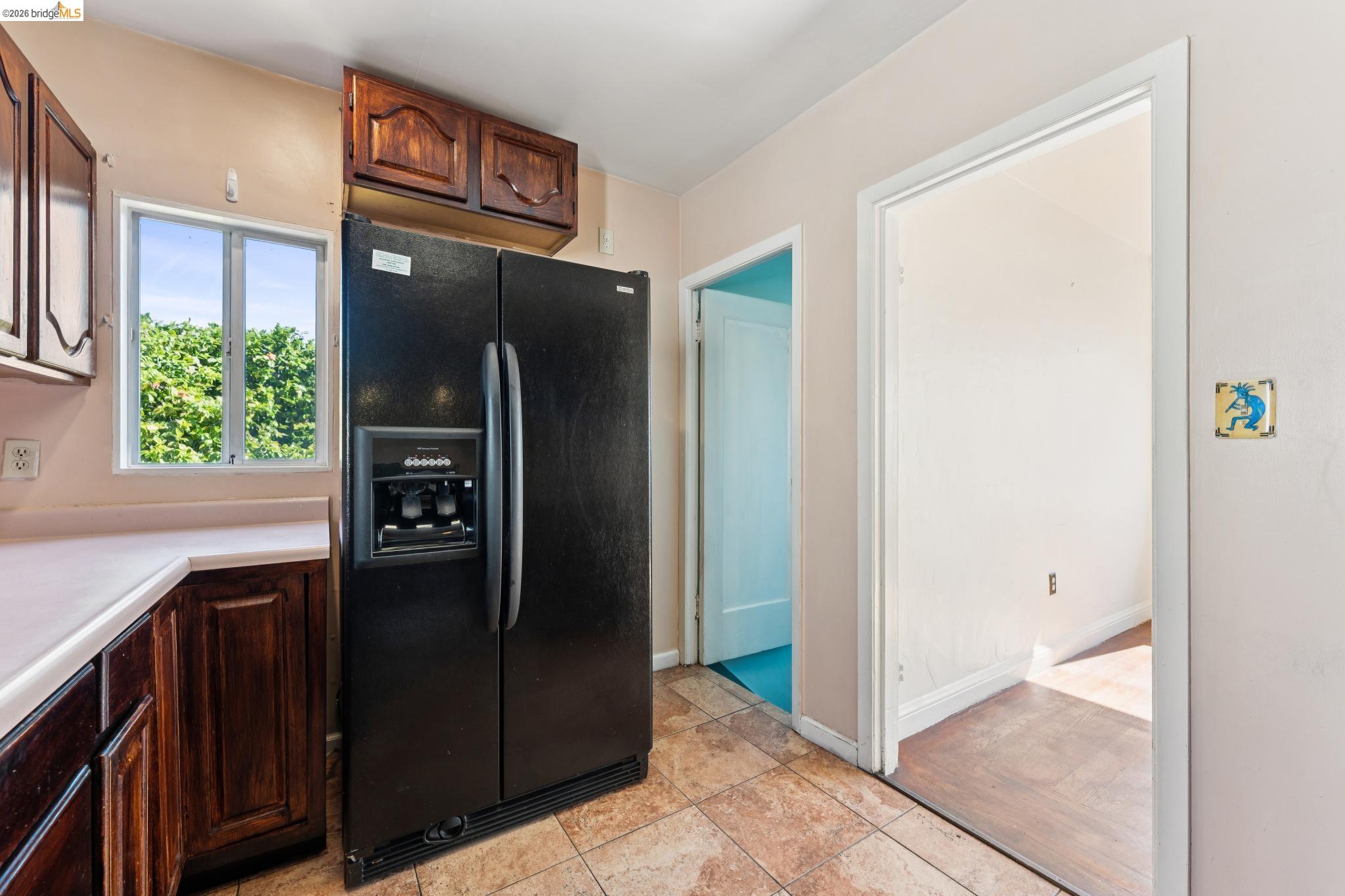 978 43rd Street Oakland, CA 94608 - Photo 20 of 46 Kitchen featuring a black side-by-side refrigerator with ice and water dispenser, wood cabinetry, light-toned countertops, and a window with exterior views
