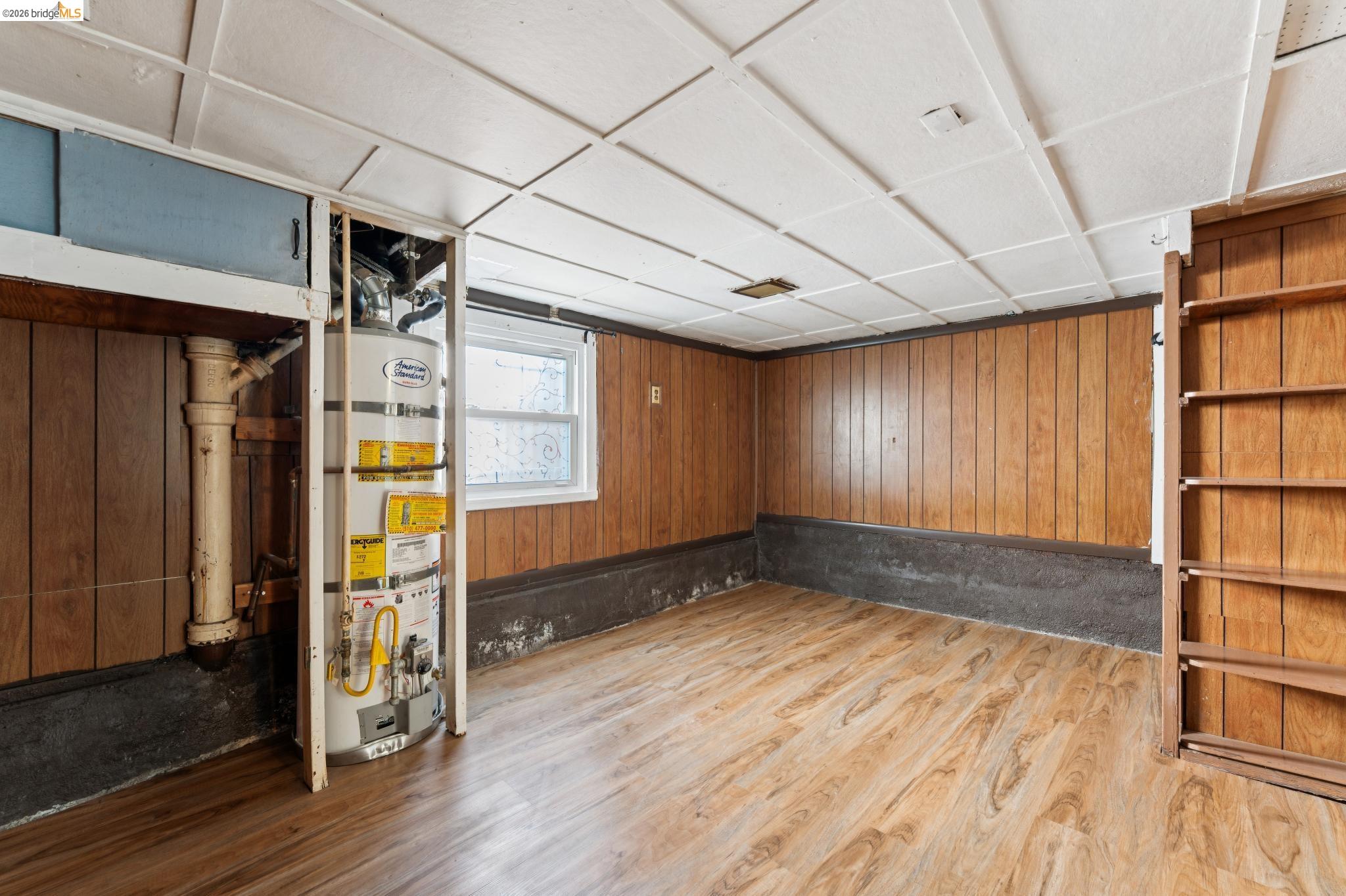 978 43rd Street Oakland, CA 94608 - Photo 30 of 46 Utility room featuring wood-finish flooring, paneled walls, a drop ceiling, built-in shelving, and a water heater