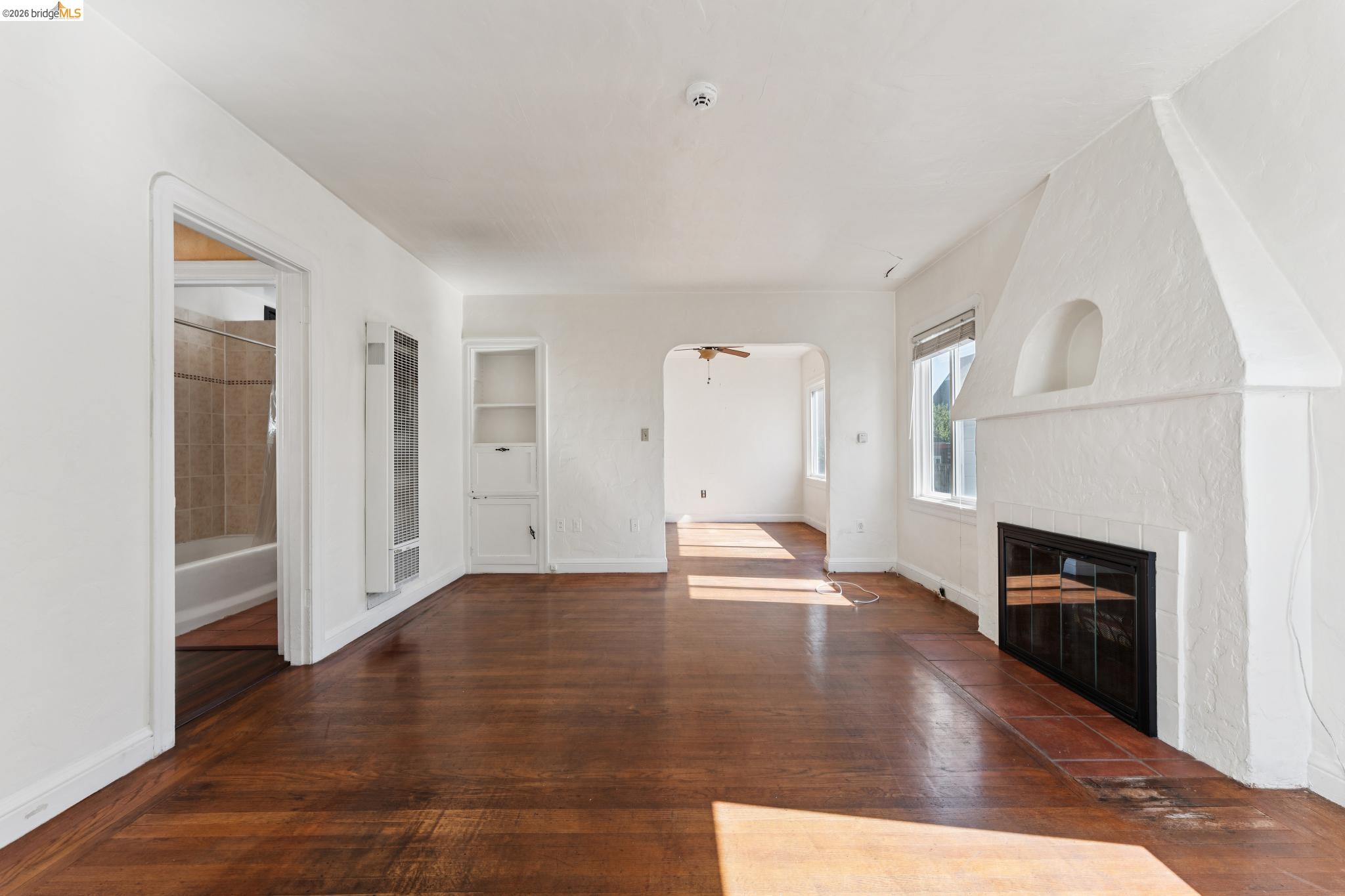 978 43rd Street Oakland, CA 94608 - Photo 7 of 46 Living area featuring wood-finish flooring, a white textured fireplace with a tile hearth, and an arched built-in niche