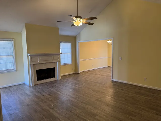 a view of an empty room with wooden floor fireplace and a window