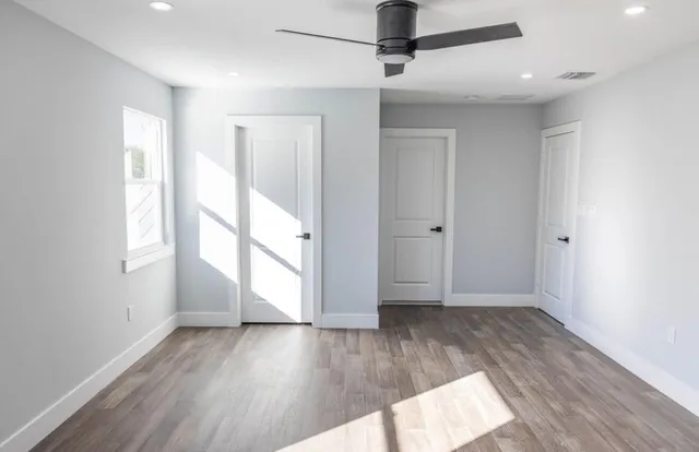 an empty room with wooden floor a ceiling fan and windows