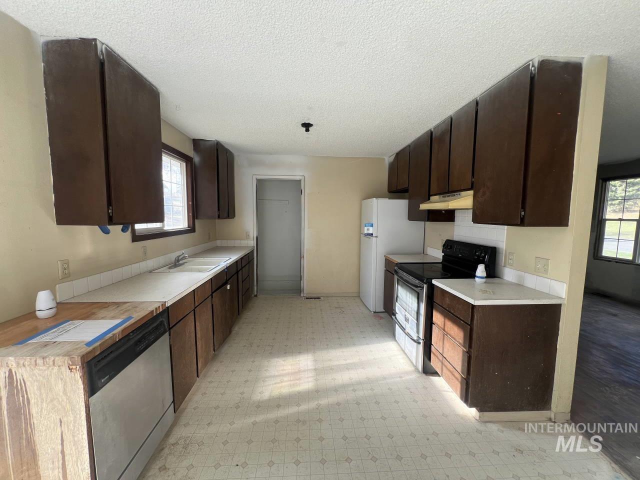 905 West Adams Street Garfield, WA 99130 - Photo 6 of 19 Kitchen with dark brown cabinets, light floors, stainless steel appliances, light countertops, and a textured ceiling