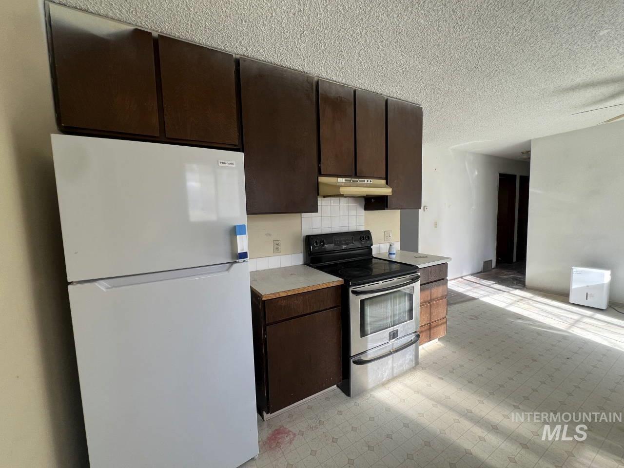 905 West Adams Street Garfield, WA 99130 - Photo 7 of 19 Kitchen with freestanding refrigerator, light floors, stainless steel range with electric stovetop, light countertops, and dark brown cabinetry