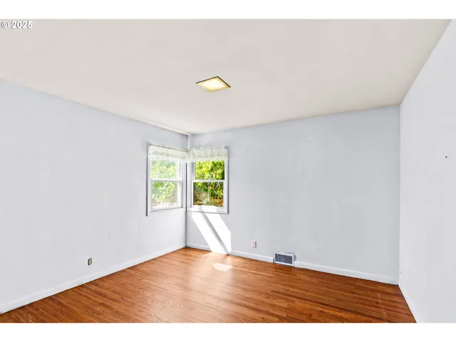a view of an empty room with window and wooden floor