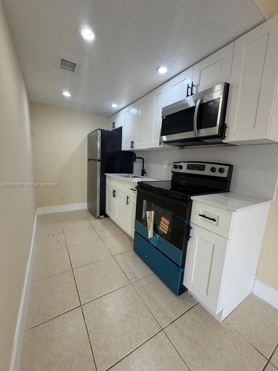 2377 West 66th Place, Unit 204 Hialeah, FL 33016 - Photo 7 of 12 a kitchen with stainless steel appliances a stove a microwave and white cabinets