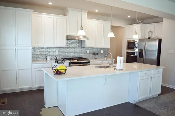 a kitchen with stainless steel appliances granite countertop a sink a stove a refrigerator a microwave oven with white cabinets