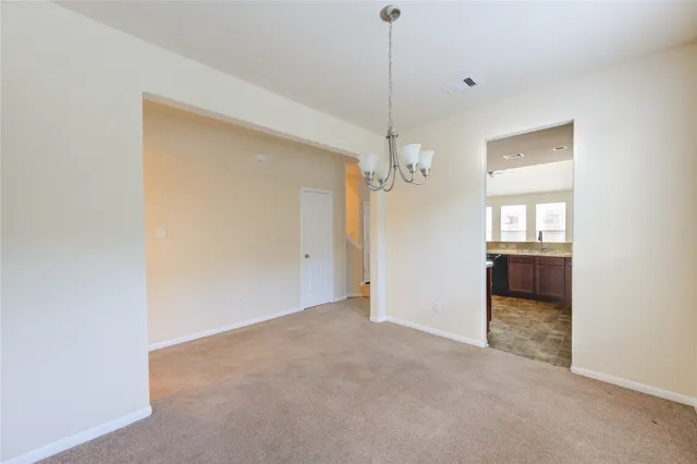 an empty room with chandelier fan and kitchen view
