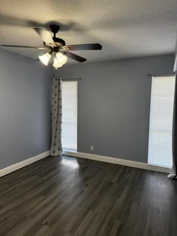 a view of an empty room with wooden floor and a fan