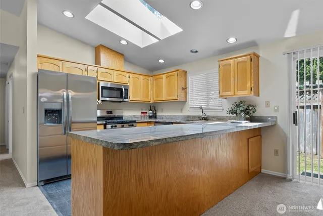 a kitchen with stainless steel appliances granite countertop a sink a stove a refrigerator cabinets and a window