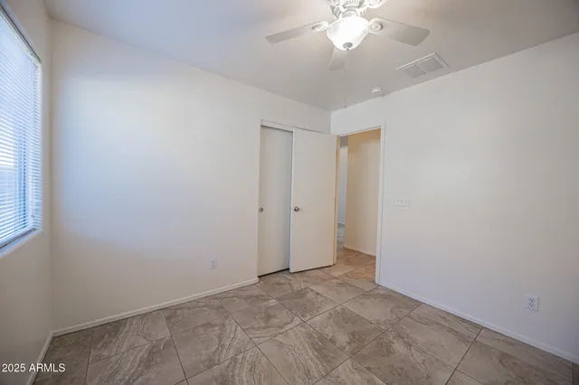 an empty room with a chandelier fan and windows
