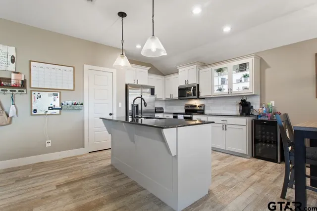 a kitchen with stainless steel appliances granite countertop a refrigerator a stove top oven a sink dishwasher and a dining table with wooden floor
