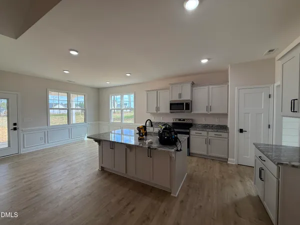 a kitchen with stainless steel appliances kitchen island granite countertop a stove top oven a sink a refrigerator white cabinets and wooden floor