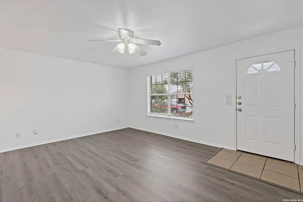 an empty room with wooden floor chandelier fan and windows
