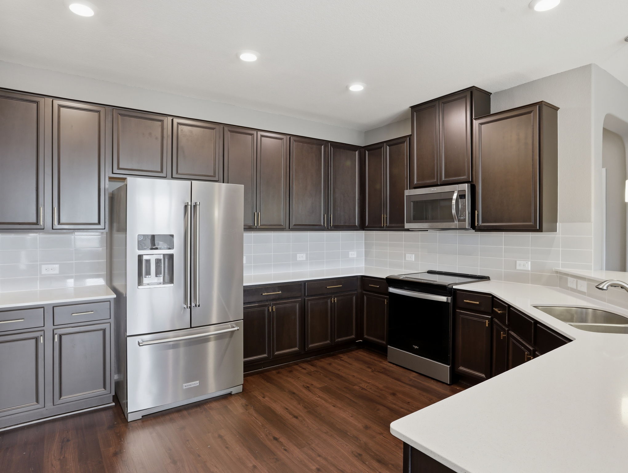 640 Landon Samuel Loop Pflugerville, TX 78660 - Photo 10 of 33 Modern kitchen featuring dark wood cabinetry, stainless steel appliances, light-toned countertops, a light gray subway tile backsplash, and wood-finish flooring