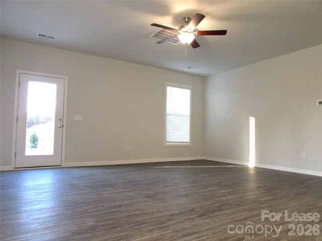 an empty room with wooden floor chandelier fan and windows