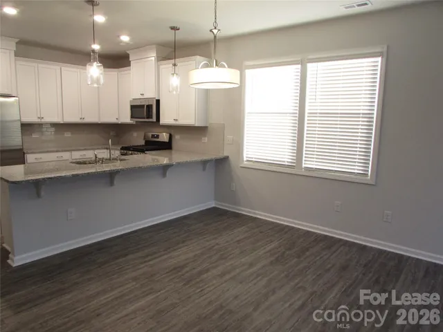 a kitchen with stainless steel appliances granite countertop a sink a stove a refrigerator and white cabinets with wooden floor