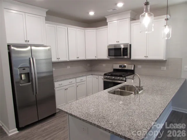 a kitchen with granite countertop a refrigerator a sink and white cabinets