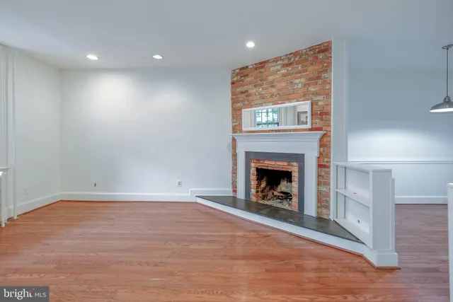 a view of an empty room with wooden floor fireplace and a window